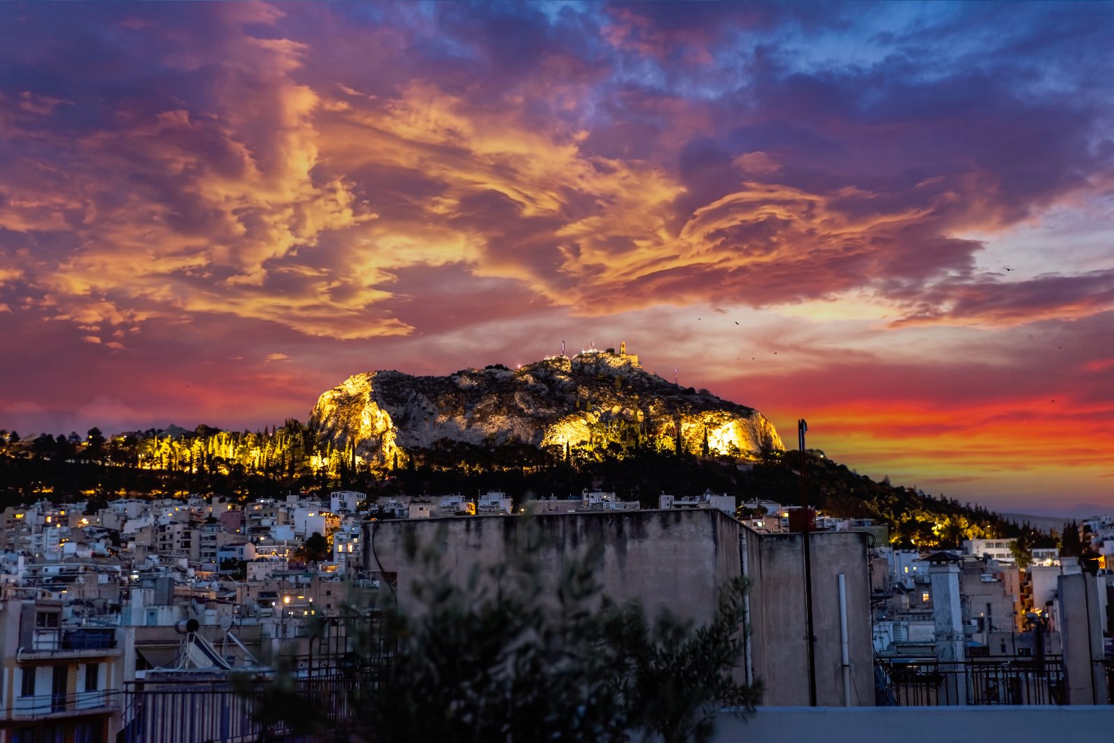 Lycabettus Hill floodlit at sunset above the Athens rooftops, seen from the shared roof terrace