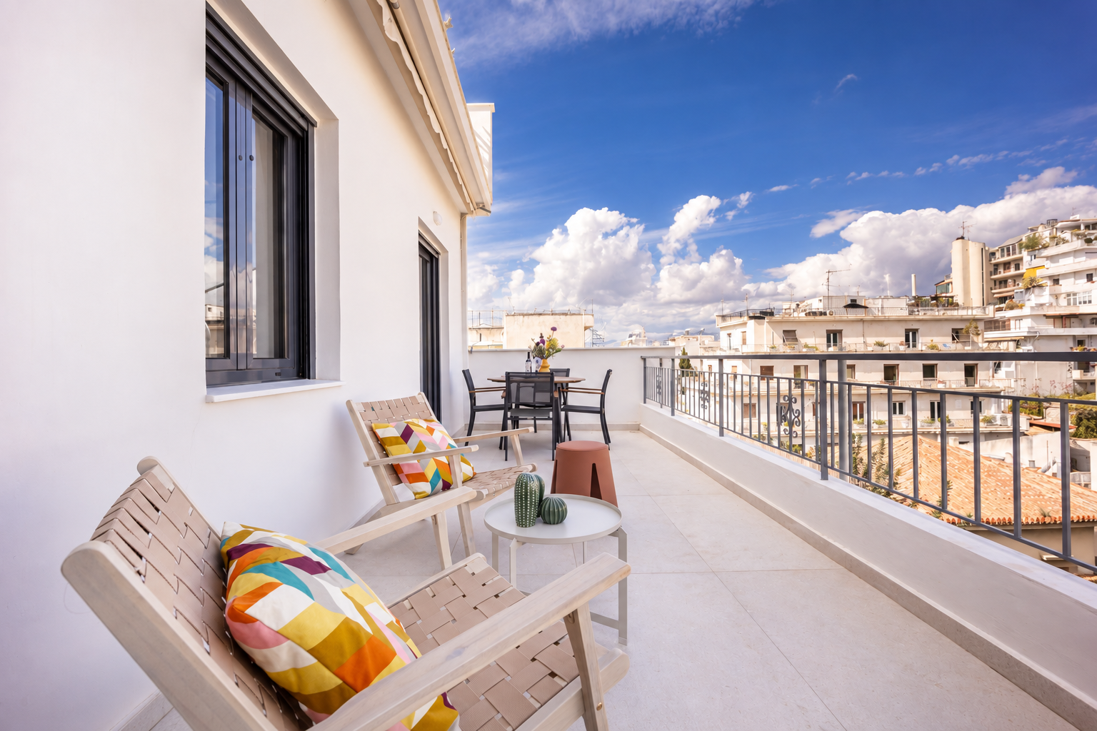 A long private terrace with woven lounge chairs, a dining table and the Exarchia rooftops beyond