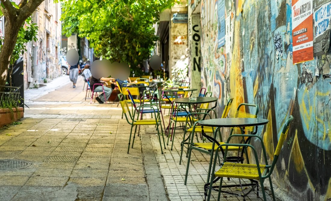 Café tables set against a graffitied wall in Exarchia